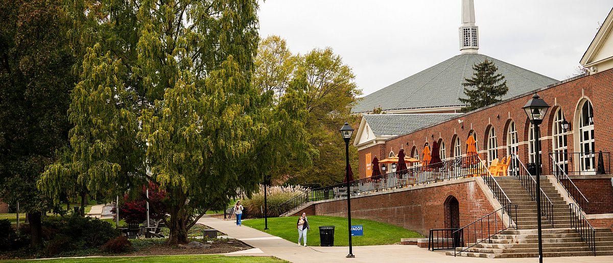 Image of campus at the start of fall. Trees are just starting to turn green to orange. Brick building to the left side of the image.